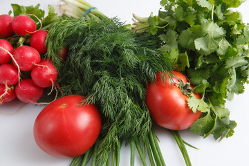 close up top view shot of a vegetable composition consisting of a bunch of radish, dill, parsley, green onions and ripe red tomatoes on a white background