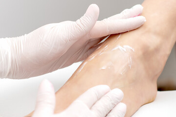 Naklejka premium Human hands in protective gloves doing foot massage with moisturizing or peeling cream in eauty salon