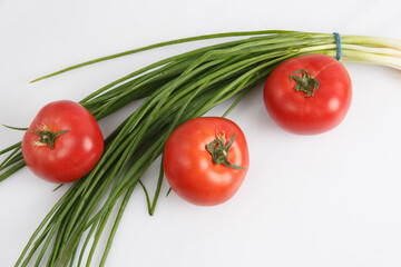 close up top view shot of a bunch of green onions and three ripe red tomato on a white background