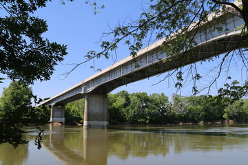 a river below a long road bridge  with bright blue sky and trees