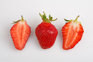 isolated close up side view shot of a row of three whole and sliced in half vibrant red strawberries on a white background