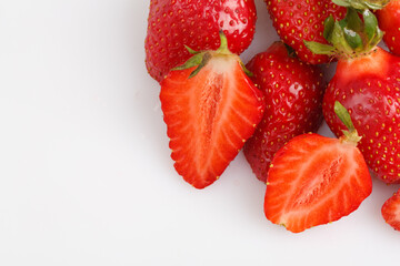 close up top view copy space shot of a bunch of whole and sliced in half vibrant red strawberries on a white background
