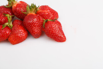 close up top view copy space shot of a bunch of whole and sliced in half vibrant red strawberries on a white background