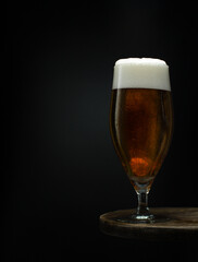 Glass of cold fresh beer with foam on wooden table on black background.Close up.