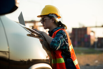 Young engineer woman standing wear safety helmet working with work by laptop evening time. blur background, concept of renewable energy and clean power.