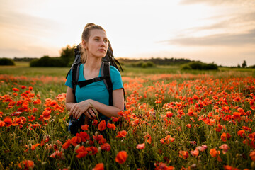 Obraz na płótnie Canvas front view of young woman tourist who stands on field of red poppies.