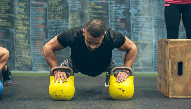 Sportsman doing push-ups with kettlebells in the gym