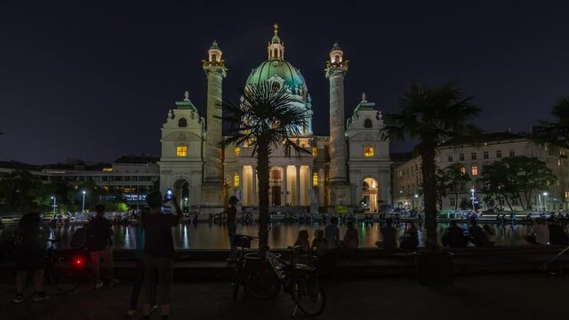 Karlskirche on the Karlsplatz square night timelapse hyperlapse in Vienna, Austria. People walking and sitting at fountain. It is a catholic church, also called Rektoratskirche, with a typical baroque