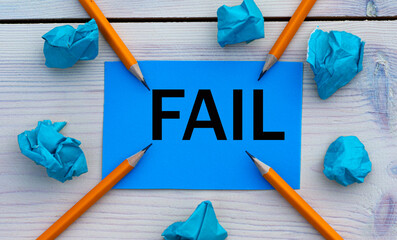 FAIL - word on blue paper on a light background with crumpled pieces of paper and pencils