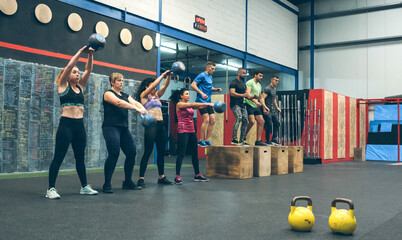 Sportswomen exercising with kettlebells and sportsmen doing box jumps