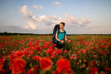 view of beauty young woman tourist who stands on field of red poppies.