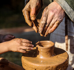 Hands of a boy and a man sculpt clay dishes.