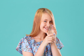 Cute teen girl with long hair smiles and drinks a glass of water on a turquoise background of the Studio