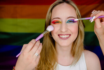 Portrait of young girl smiling while being made up in bright colors with the background of the rainbow flag of gay pride