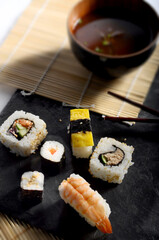 Image of sushi with chopsticks, in the background there is some miso soup. 
