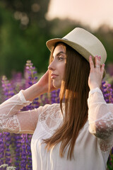 A girl with her hair in a lupine field looks at the setting sun and her profile is highlighted by the sun.