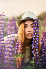 A brunette with her hair in a summer hat is standing in a field among flowers