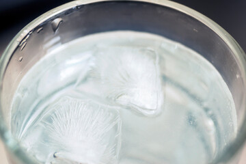 Water in a glass with ice Sea lay a wooden floor. Focus on the ice behind the blur and poor light.