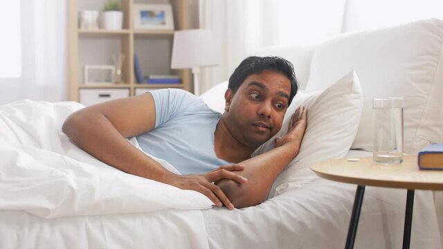 people, bedtime and rest concept - indian man lying in bed and dropping medicine pill into glass of water at home