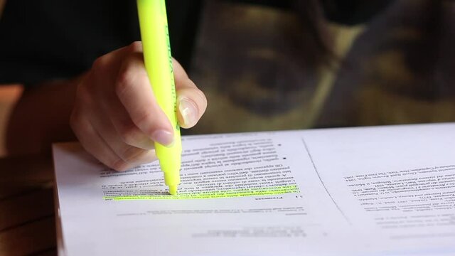 Female hand holding highlighter pen, highlighting important texts in study.