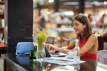  young female brunette looking at her laptop, smiling with headphones in her ears