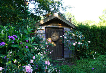 Fototapeta na wymiar Flowers and plants planting farm garden with little small cottage or shed. Nice green natural gardening concept. Look like a nice english green garden.