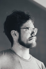 a handsome young man with a thick beard and glasses is illuminated on one side by a soft light. fashionable beard, happy. reflection in the mirror. irritation after shaving