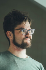 a handsome young man with a thick beard and glasses is illuminated on one side by a soft light. fashionable beard, happy. reflection in the mirror. irritation after shaving