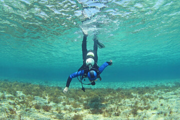 A scuba diver dives from the surface to the bottom. The diver begins his dive underwater
