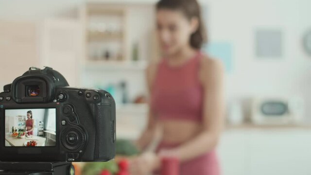 Close up of camera display recording video of young Caucasian sporty woman standing at kitchen worktop and making healthy breakfast