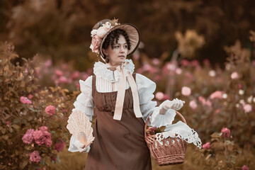 Outdoor close up portrait of beautiful woman wearing wide brim ribbon tie straw hat, vintage dress. Model posing in the blooming rose garden.