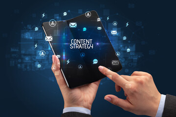 Businessman holding a foldable smartphone with CONTENT STRATEGY inscription, social networking concept