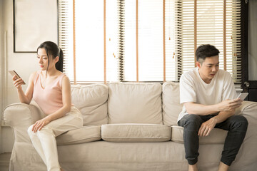 Couples are using mobile phones sitting on the sofa and keeping social distance