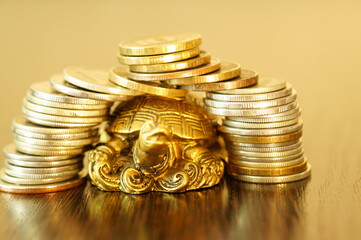 Metal turtle with coins on a gold background. The coins are arranged in the form of a turtle house.