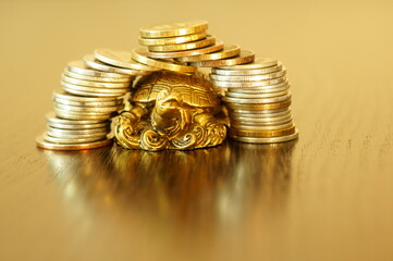 Metal turtle with coins on a gold background. The coins are arranged in the form of a turtle house.