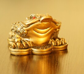 A metal toad with a coin in its mouth on a gold background.