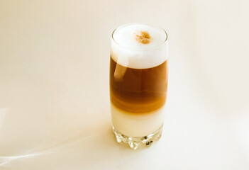 Coffee latte with white foam poured in layers in a transparent glass. A tall glass on a white background.