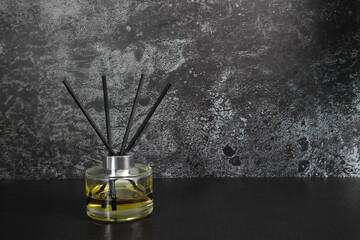 The luxury scented aroma room fresherner reed diffser sticks glass bottle with black fiber sticks is on the black table to creat relax ambient with background of black marble wall in the living room