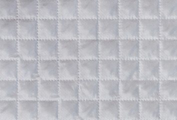 White cloth or material texture with checkered structure or embossing. Synthetic fabric pattern or background. Macro, close up shot.