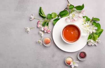 Chocolates of various colors in a festive elegant box packing a cup of tea on pastel pink background decoration flowers.