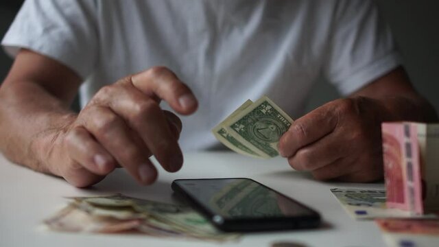 Man counting money savings due to economic financial crisis and unemployment looking at phone with currency rates and a calculator, income decrease