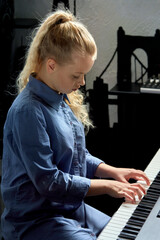 Vertical photo of a beautiful blonde girl who is learning to play the piano. © Evgenia
