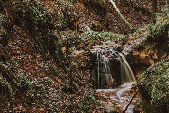 Small creek waterfall in a beautiful deciduous autumn forest. Beautiful autumn landscape. Long exposure.