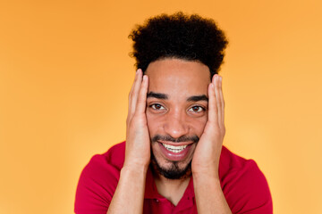 Close up indoor portrait of happy handsome afro american man wearing red t-shirt smiling at camera over orange background 