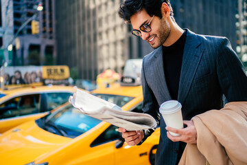 Smiling successful entrepreneur in elegant suit satisfied with article in daily press standing on...