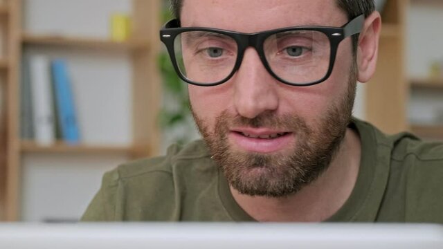 A close-up view of a handsome young businessman wearing glasses is working with his laptop sitting at the table in the office