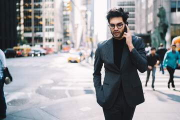 Busy entrepreneur in trendy formal wear having mobile phone conversation strolling on avenue in New York downtown,handsome businessman calling for consultation operator making banking