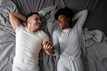 Multiethnic couple lying in bed and looking each other and smile