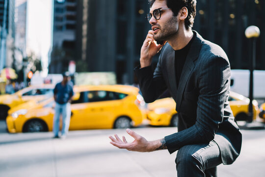 Cropped image of angree male lawyer dressed in stylish formal wear solving financial problems during serious mobile conversation on smartphone device standing in downtown of metropolis