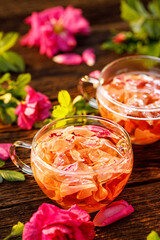 Rose tea infusion of rose petals in a glass cups among fresh rose flowers on a wooden table close up view